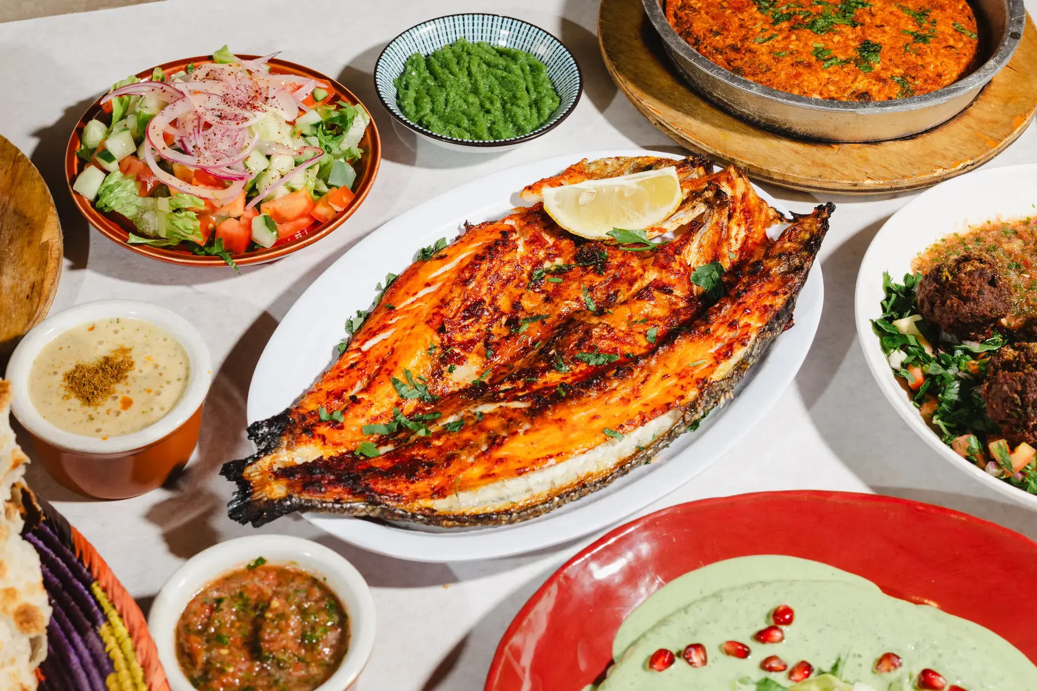 An overhead spread of Yemeni Palace dishes: grilled fish, saltah, sahawiq, salads, soup, and fresh bread.